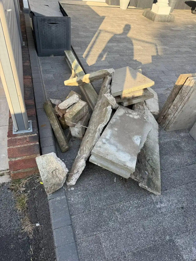 Broken paving slabs and rubble piled on a driveway before clearance